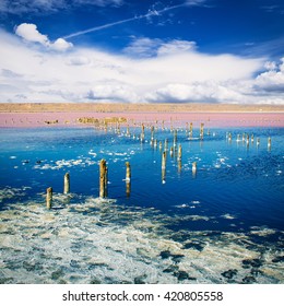 Beautiful salt lake with blue and pink water,  white clouds  and wooden posts, natural landscape amazing background