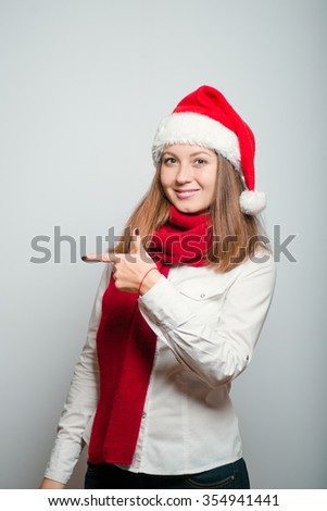 beautiful santa girl points to someone in the side. Christmas hat isolated portrait of a woman on a gray background, studio photo.
