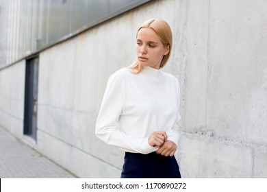 Beautiful Scandinavian woman standing near grey wall, street style urban city style, autumn clothes white sweater, casual wear, fashion model posing for photo on magazine. Confident and strong.