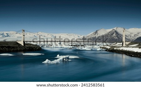 A beautiful scene of the bridge over the frozen lake surrounded by snow-covered mountains in Jokullsar, Iceland