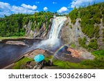 Beautiful scenery landscape view of Montmorency Falls and magnificent rainbow against mountain, bridge, blue sky, clouds in Montmorency Falls Park, Quebec, Canada. Large waterfall on Montmorency River