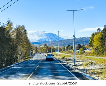 Beautiful scenic route winding through vibrant autumn scenery towards a majestic snow-capped mountain summit against a backdrop of clear blue skies - Powered by Shutterstock