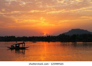 Beautiful scenic view - colorful sunset above calm water of Dal Lake with dramatic cloudy sky and traditional boat (shikara) shadow figures, Srinagar, Jammu & Kashmir, Northern India, Central Asia