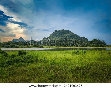 A beautiful Scenic view of the mountain with green grass and a calm lake with cloudy blue sky background at tasik timah tasoh, perlis, malaysia.
