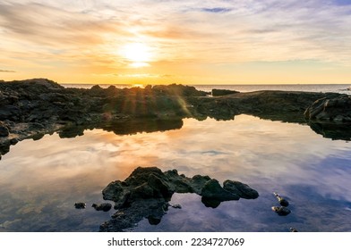 beautiful sea sunrise on a rocky sea coast with calm water , amazing cloudy sky and reflection on water surface