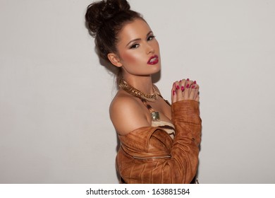 Beautiful Seductive Elegant Woman In A Leather Jacket And Jewellery With Her Hair In A Bun Posing On A Grey Studio Background