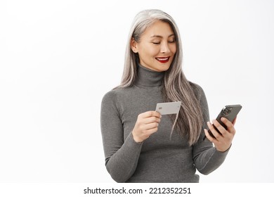 Beautiful Senior Asian Woman Using Mobile Phone, Holding Credit Card, Order Or Shopping Online, Standing Happy Over White Background