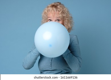 Beautiful senior blonde woman preparing for party blowing up blue balloon