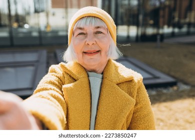 Beautiful senior blonde woman taking selfie on sity street. Looking at camera and smile. Travel and active life concept. Outdoors - Powered by Shutterstock