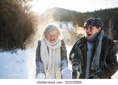 Beautiful senior couple blowing snow in sunny winter nature