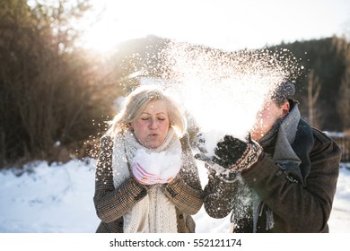 Beautiful Senior Couple Blowing Snow In Sunny Winter Nature