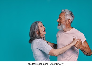 Beautiful senior couple dancing and smiling while standing together against blue background - Powered by Shutterstock