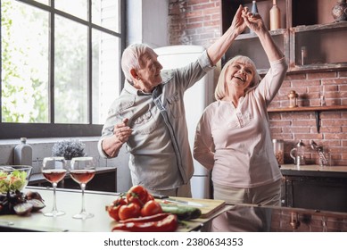 Beautiful senior couple is dancing and smiling while cooking together in kitchen - Powered by Shutterstock