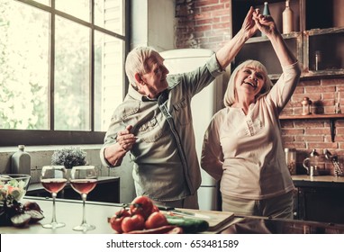 Beautiful senior couple is dancing and smiling while cooking together in kitchen - Powered by Shutterstock