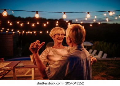 Beautiful Senior Couple Dancing Together In Their Backyard Decorated With Lamps