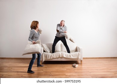 Beautiful senior couple having a pillow fight. Studio shot. - Powered by Shutterstock