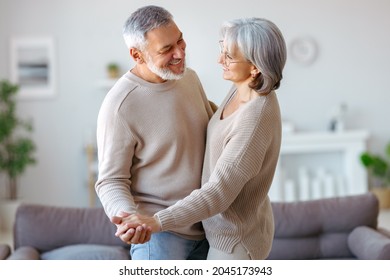 Beautiful senior couple in love looking at each other with tenderness while dancing together in living room at home, two pensioners wife and husband enjoying happy life moments on retirement - Powered by Shutterstock