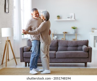 Beautiful senior couple in love looking at each other with tenderness while dancing together in living room at home, two pensioners wife and husband enjoying happy life moments on retirement