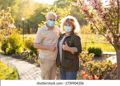 Beautiful Senior Couple In Love Wearing Medical Mask To Protect From Coronavirus And Showing Thumbs Up Outside In Spring Or Summer Nature