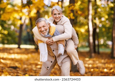 Beautiful senior couple in park on autumn day, two pensioners:   husband  giving piggyback ride to happy  wife while ejoying happy life moments on retirement on walk outdoors
 - Powered by Shutterstock