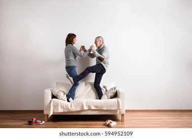 Beautiful Senior Couple Standing On Couch, Dancing. Studio Shot.