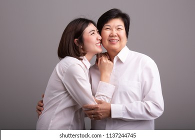 Beautiful senior mom and her adult daughter are hugging, looking at camera and smiling
