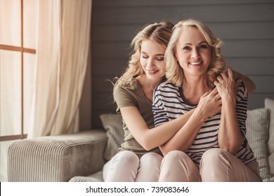 Beautiful Senior Mom And Her Adult Daughter Are Hugging And Smiling While Sitting On Couch At Home