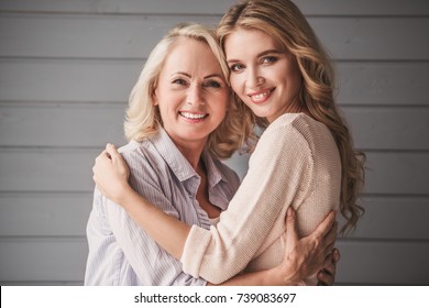 Schöne ältere Mutter und ihre erwachsene Tochter umarmt, sehen Kamera und lächeln