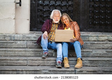 Beautiful Senior Multiethnic Elderly Couple Using Technology, Computer Sitting On Stairs In The City At Night. Asian Male African American Woman