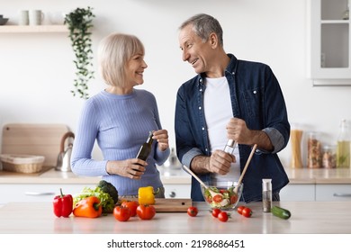 Beautiful Senior Spouses Making Healthy Dinner Together At Home, Happy Elderly Husband And Wife Cooking Meal And Having Conversation, White Cozy Kitchen Interior, Copy Space