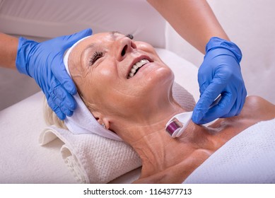 Beautiful Senior Woman In Beauty Salon During Anti Aging Procedure With Derma Roller