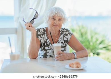 Beautiful senior woman with a cup of coffee with milk resting in nature at the resort in the morning. Vacation, holiday, and travel concept. - Powered by Shutterstock