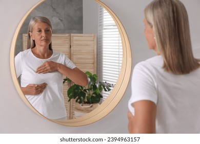 Beautiful senior woman doing breast self-examination near mirror in bathroom - Powered by Shutterstock