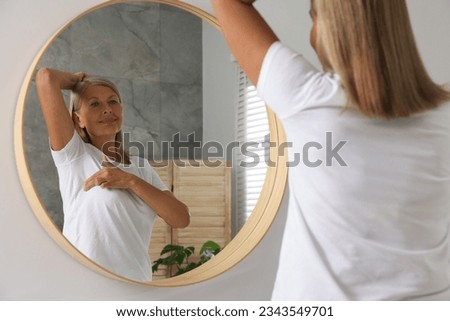Beautiful senior woman doing breast self-examination near mirror in bathroom