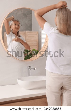 Beautiful senior woman doing breast self-examination near mirror in bathroom