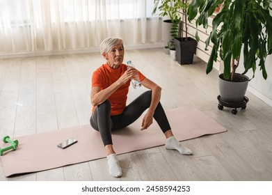 Beautiful senior woman drinking water after exercise. Active senior woman practicing yoga indoors. Exercise for Older Adults - Powered by Shutterstock