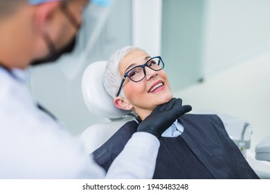 Beautiful Senior Woman Having Dental Treatment At Dentist's Office. Dentist Is Wearing Protective Face Mask And Shield Due To Coronavirus Pandemic.	