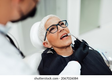 Beautiful Senior Woman Having Dental Treatment At Dentist's Office. Dentist Is Wearing Protective Face Mask Due To Coronavirus Pandemic.	