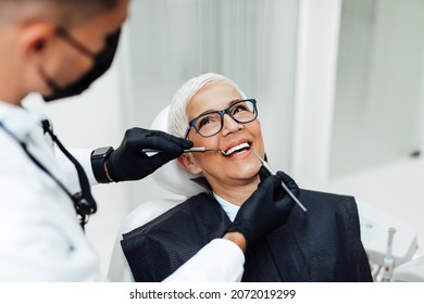 Beautiful senior woman having dental treatment at dentist's office. Dentist is wearing protective face mask due to coronavirus pandemic.	 - Powered by Shutterstock