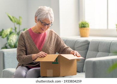 Beautiful senior woman is holding cardboard box sitting on sofa at home. - Powered by Shutterstock