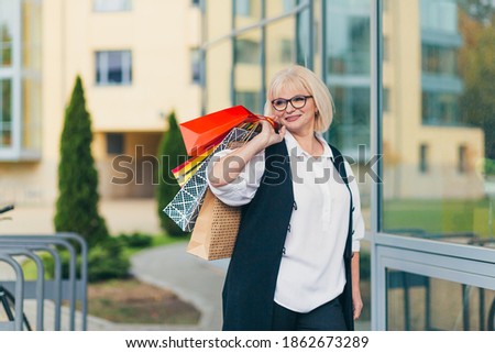 Beautiful senior woman holding colored bags for goods and gifts on the background of the supermarket