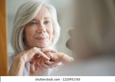 Beautiful senior woman infront of mirror with make up brushes                         - Powered by Shutterstock