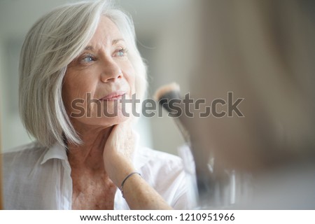 Beautiful senior woman infront of mirror with make up brushes                        