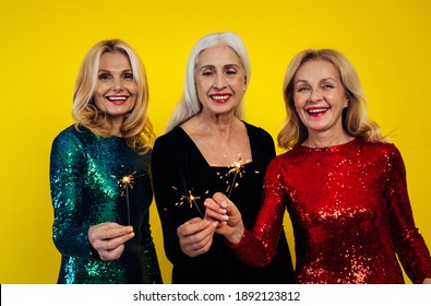 Beautiful Senior Woman Making Party And Celebrating New Year. Middle Aged Women Wearing Elegant Glittering Dresses And Having Fun. Studio Portraits On Colored Background