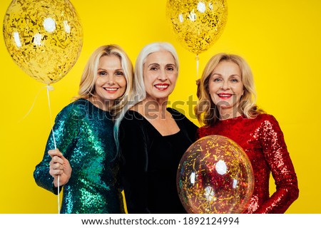 Beautiful senior woman making party and celebrating new year. Middle aged women wearing elegant glittering dresses and having fun. Studio portraits on colored background