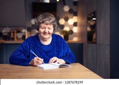 Beautiful Senior Woman In Modern Home Writing Down Expenses