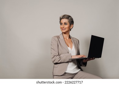 Beautiful Senior Woman Smiling And Posing With Laptop Isolated Over Beige Background