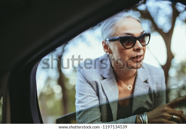 Beautiful senior woman talking with taxi driver\
through opened car window. Businesswoman in sunglasses talking with\
cab driver.