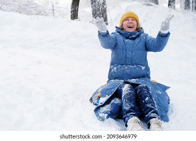 Beautiful Senior Woman In Yellow Hat And Blue Coat Throws Snow Up.