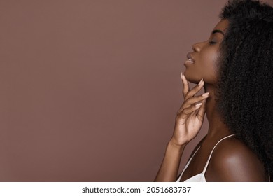 Beautiful sensual sexy young black African ethnic woman model posing profile side face touching chin on brown background advertising facial neck skin care spa treatment, nails manicure and skincare.